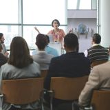 businesswoman-speaking-animatedly-to-crowd-of-business-people-at-business-seminar-in-office.jpg