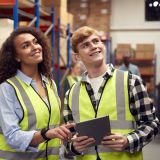 male-intern-with-team-leader-looking-at-digital-tablet-inside-busy-warehouse-facility-e1702366539748.jpg