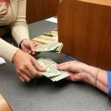 womans-hand-reaches-for-money-from-teller-at-the-bank-for-vacation-cash-and-spending-money-e1706687781799.jpg