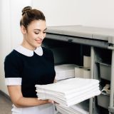 young-happy-maid-in-uniform-taking-towels-from-shelf-of-housekeeping-cart.jpg